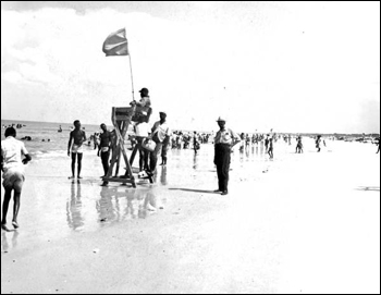 White peace officer, right, standing by the lifesaving station at Butler Beach: Anastasia Island, Florida (195-)