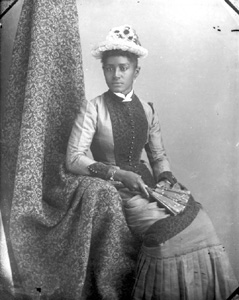 Seated woman wearing sunflower hat, holding a fan