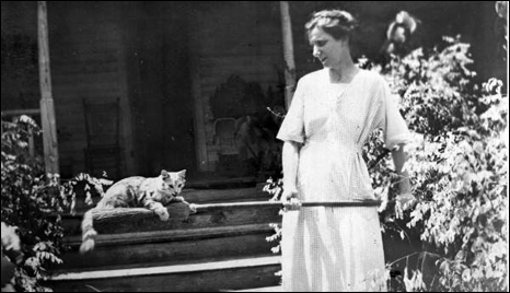 Woman holding a broom with cat lying on it (1918)