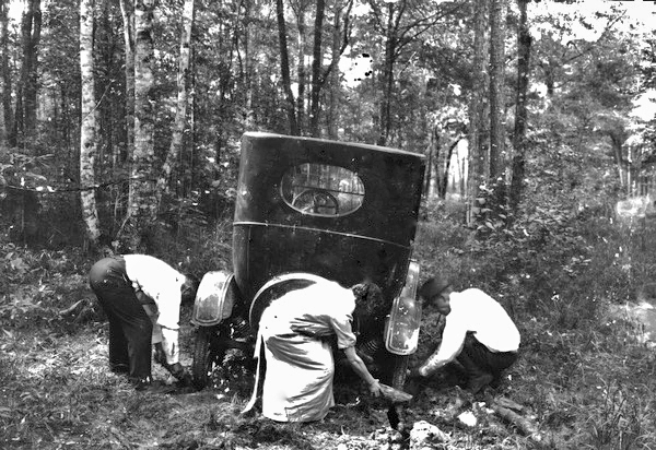 These travelers struggle to free their car from the mud along a wooded stretch of early Florida roadway (circa 1924).