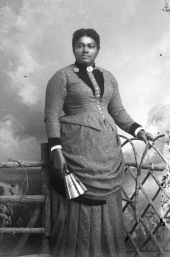 Woman holding fan at a gate.