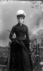 Woman wearing beaded dress and hat with feather.