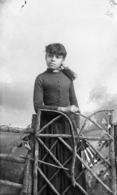 Girl holding a fan standing behind a gate.