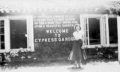 Unidentified lady stands in front of the sign for Cypress Gardens - Winter Haven, Florida