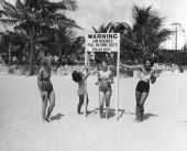 Young women making fun of sign at beach requiring full bathing suits - Miami, Florida.